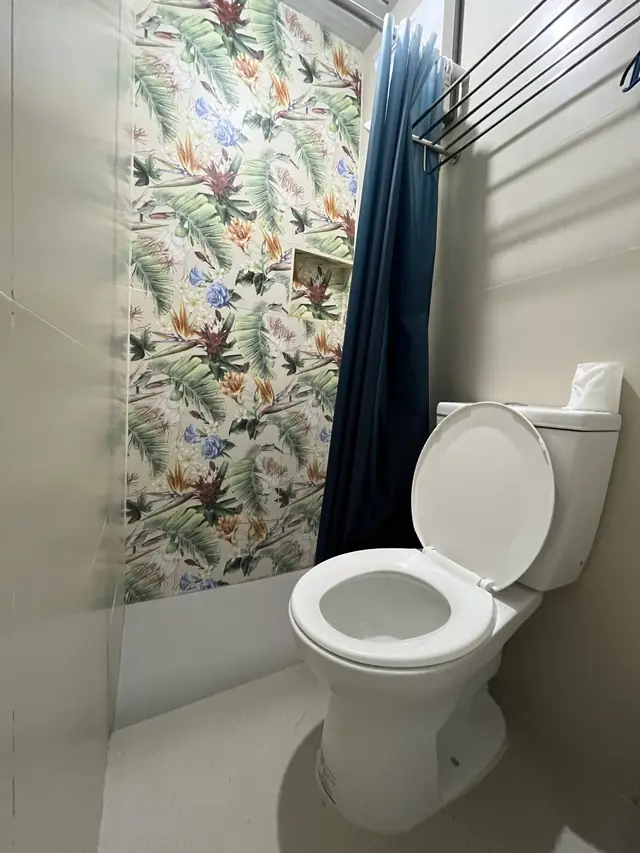 Toilet with tropical leaf tiles and blue shower curtain